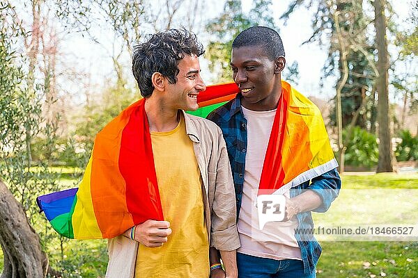 Multiethnisches schwules männliches Paar  das eine Regenbogenflagge mit dem Symbol der Homosexualität hält und Spaß hat