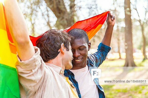 Multiethnisches schwules männliches Paar  das eine Regenbogenflagge mit dem Symbol der Homosexualität hält  romantische Pose