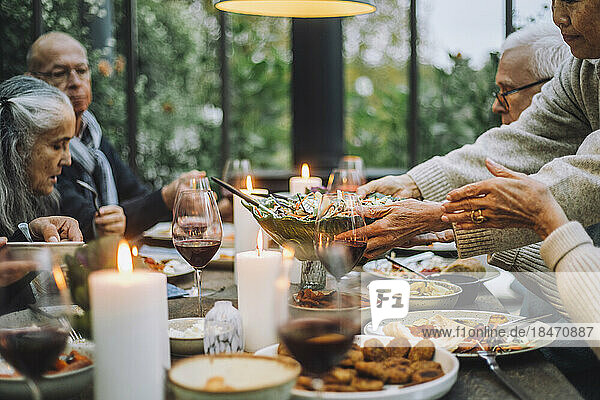 Ältere Frau serviert Salat für männliche und weibliche Freunde während einer Party