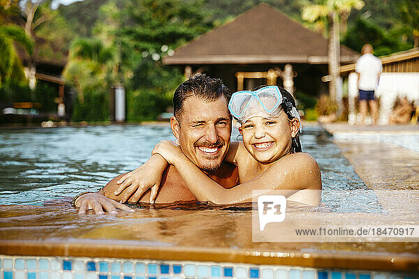 Porträt einer lächelnden Tochter und eines Vaters im Schwimmbad eines Ferienortes