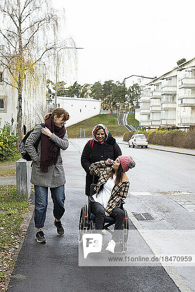 Mutter und Krankenschwester sprechen mit einer Frau  die im Rollstuhl sitzt  während sie auf dem Bürgersteig spazieren geht