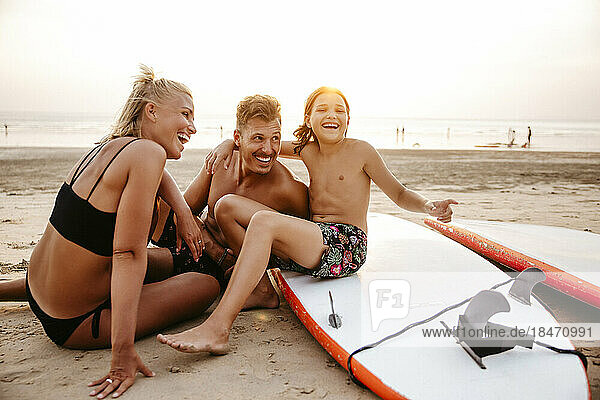 Cheerful parents enjoying with daughter sitting on paddleboard at beach during sunset