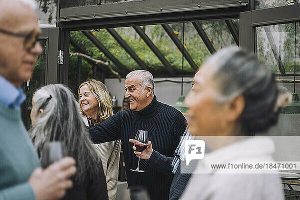Glücklicher reifer Mann genießt mit älteren männlichen und weiblichen Freunden während einer Dinnerparty im Hinterhof
