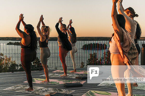 Weibliche Freunde üben zusammen auf der Terrasse bei Sonnenuntergang eine Baumpose