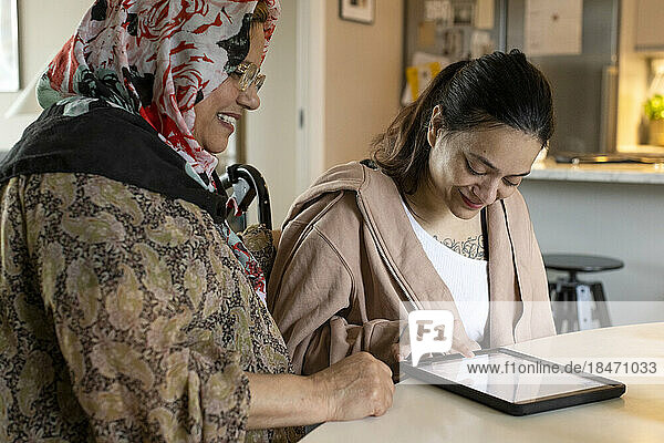 Frau mit Behinderung benutzt Tablet-PC bei ihrer Mutter zu Hause