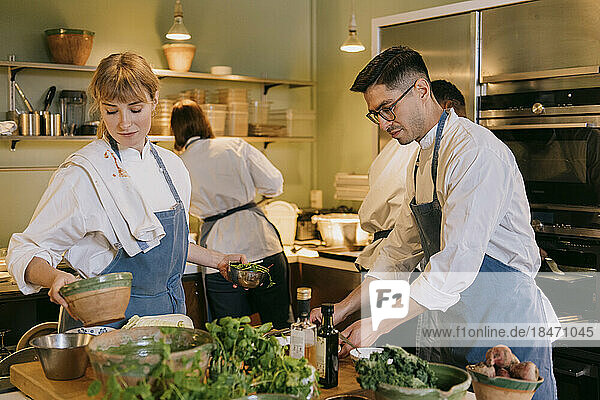 Männlicher und weiblicher Koch helfen sich gegenseitig bei der Zubereitung von Speisen in einer Großküche