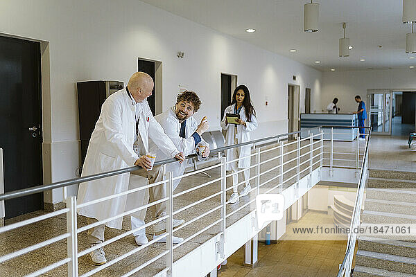 Lächelnde männliche Ärzte  die sich in der Kaffeepause mit einer weiblichen Kollegin auf dem Krankenhausflur unterhalten