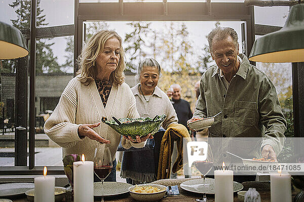 Männliche und weibliche ältere Freunde helfen sich gegenseitig beim Eindecken des Tisches während einer Dinnerparty