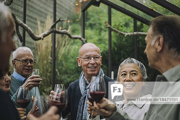 Lächelnder älterer Mann im Gespräch mit männlichen und weiblichen Freunden im Ruhestand auf einer Party