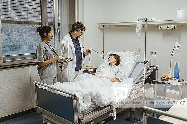 Healthcare workers talking to senior female patient lying on bed in hospital