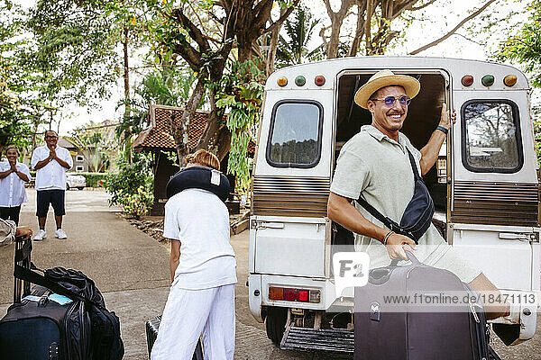 Lächelnder männlicher Tourist  der mit seinem Gepäck aus dem Van am Urlaubsort aussteigt