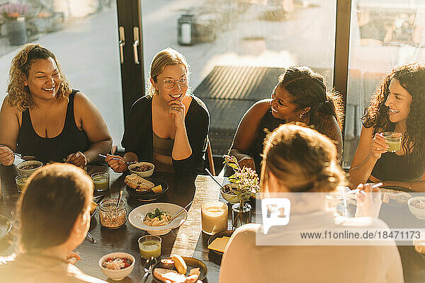 Frau mit Hand am Kinn im Gespräch mit Freundinnen beim Frühstück im Freizeitzentrum