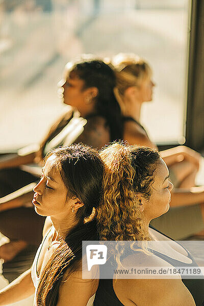 Women friends sitting back to back and exercising during yoga class
