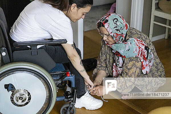 Mutter bindet die Schnürsenkel ihrer Tochter  die zu Hause im Rollstuhl sitzt