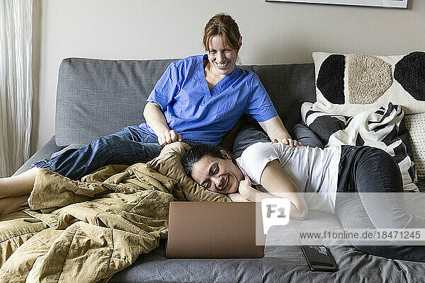 Betreuerin und Frau mit Behinderung sehen sich zu Hause einen Film auf dem Laptop an