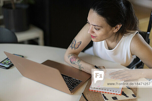 Frau mit Querschnittslähmung schreibt in Tagebuch und schaut auf Laptop