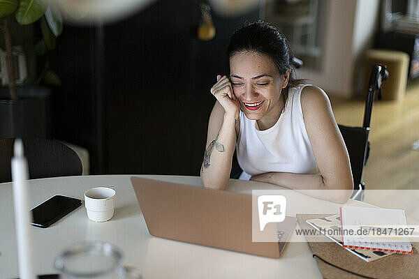 Glückliche Frau mit Querschnittslähmung genießt es  zu Hause den Laptop zu beobachten