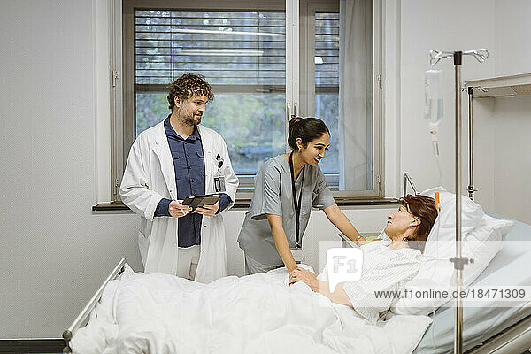 Lächelnde Krankenschwester im Gespräch mit einem älteren Patienten  der auf dem Bett eines Arztes im Krankenhaus liegt