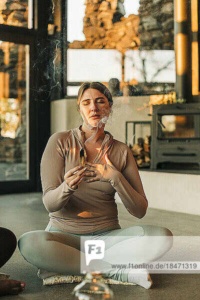 Frau mit Hand auf der Brust  die brennendes Sandelholz hält  während sie in einem Rückzugszentrum meditiert