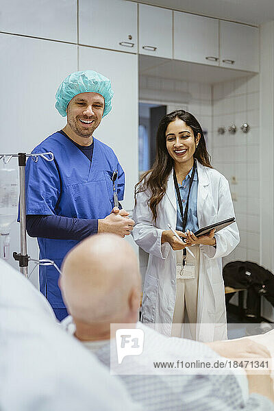 Fröhliches Gesundheitspersonal im Gespräch mit einem älteren männlichen Patienten im Krankenhaus