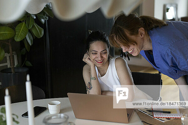 Krankenschwester und querschnittsgelähmte Frau schauen zu Hause gemeinsam auf den Laptop