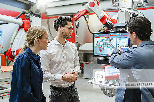 Engineer explaining colleagues over monitor at robot factory