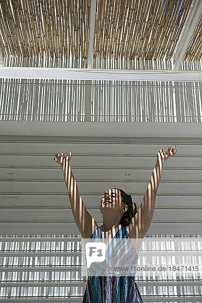 Smiling woman with arms raised enjoying in sunlight