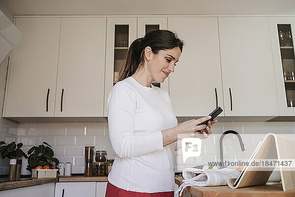 Lächelnde Frau benutzt Smartphone in der heimischen Küche