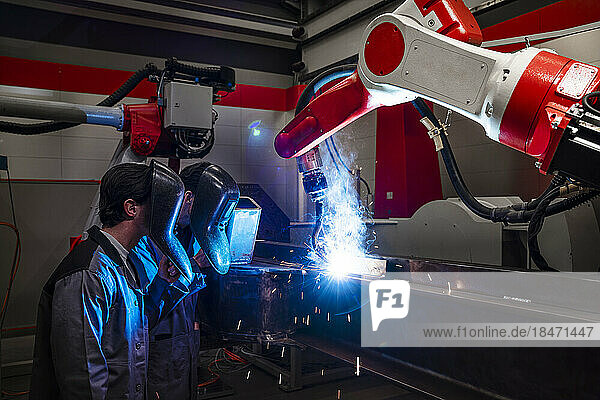 Engineers wearing protective workwear by robotic arm welding in factory