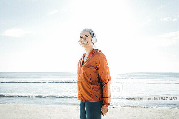 Smiling mature woman wearing headphones listening to music at beach