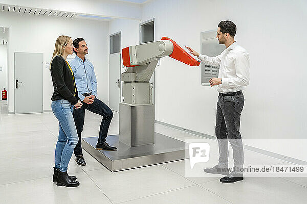 Engineer explaining robotic arm to colleagues standing at factory