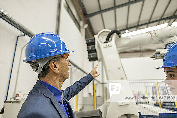 Mature businessman pointing at robotic arm in factory
