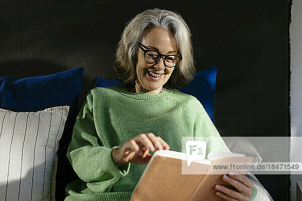 Smiling mature woman reading book in bedroom