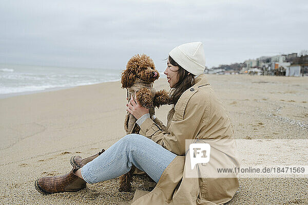Frau genießt es  mit Hund am Strand zu sitzen