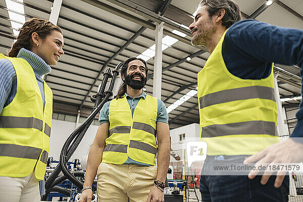 Happy engineers wearing reflective clothing talking with each other in factory