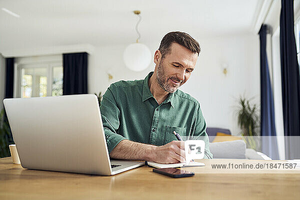 Handsome man working from home taking notes at desk