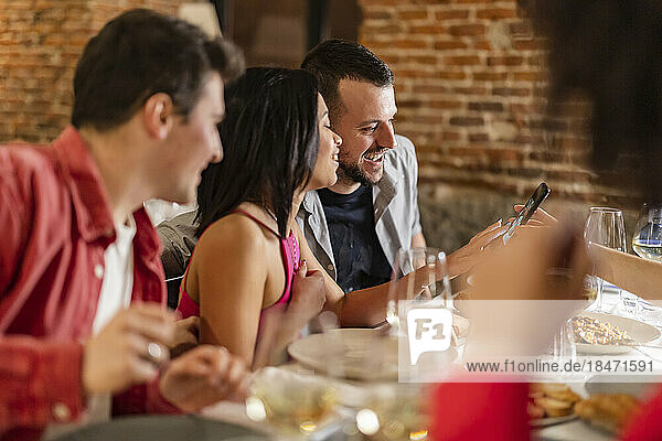 Young woman sharing smart phone with friends at dinner party