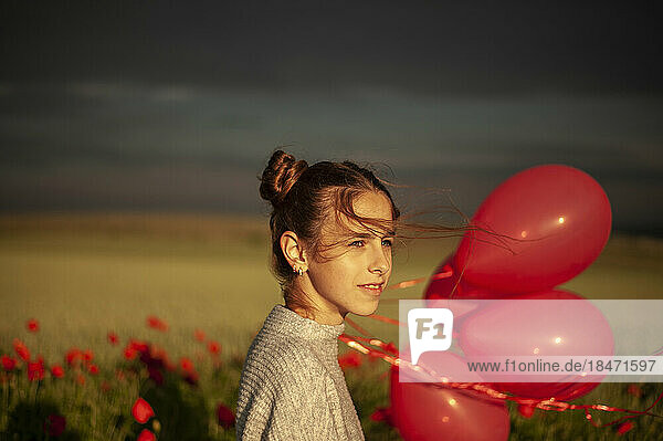 Contemplative smiling girl standing with balloons at poppy field