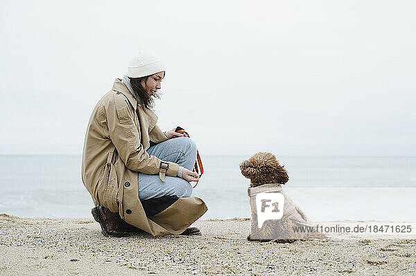 Junge Frau kauert neben Hund am Strand