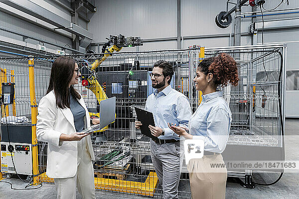 Smiling businesswoman holding laptop and having discussion with colleagues in factory