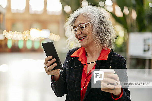 Happy businesswoman holding disposable coffee cup using smart phone