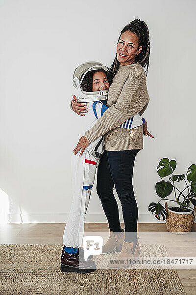 Smiling girl wearing space suit embracing mother standing at home