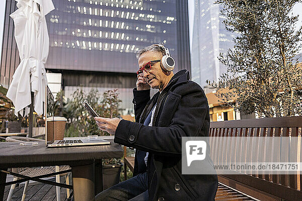 Businessman wearing wireless headphones using smart phone at table