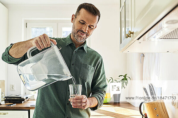 Man pouring water from a filter jug into a glass in the kitchen