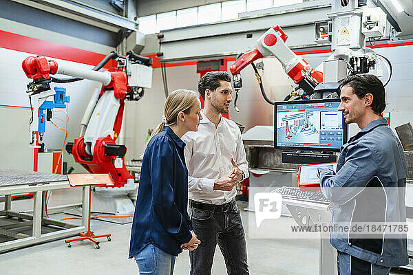 Colleagues discussing together standing at robot factory