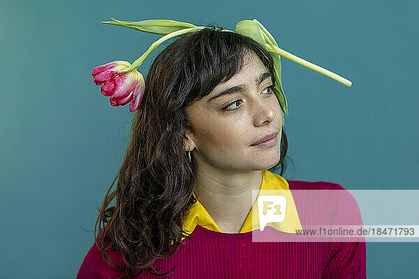 Nachdenkliche Frau mit Tulpe auf dem Kopf vor grünem Hintergrund