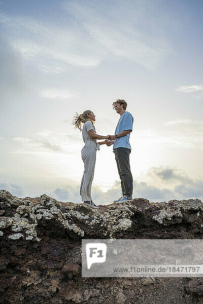 Young couple standing on cliff holding hands