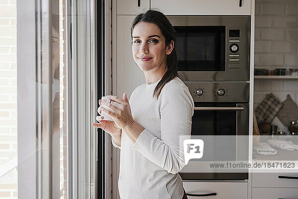 Smiling woman holding coffee cup standing by window