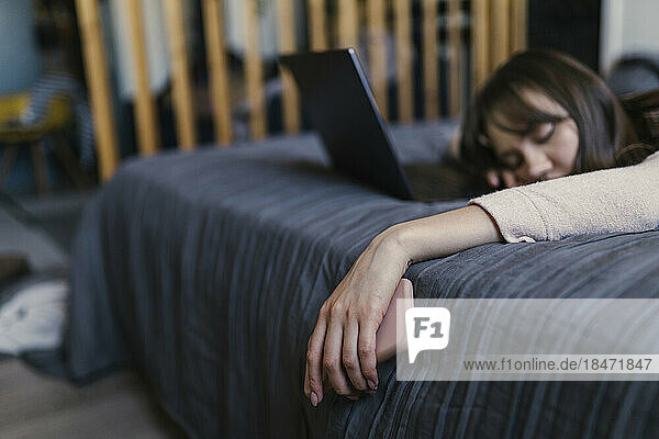 Tired young woman holding smart phone lying on bed at home