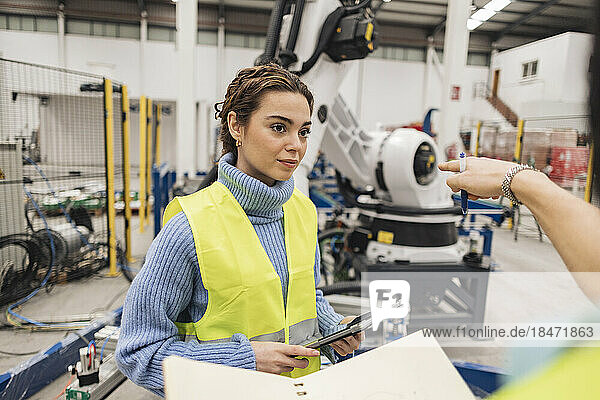 Engineer gesturing colleague with tablet PC in robotics factory